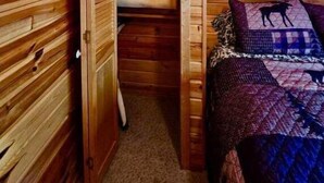 Een houten blokhut van binnen, met een bed, een kast en een lijst met een afbeelding aan de muur.