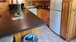 Een keuken met houten kastjes, een granieten aanrecht, een fornuis, een magnetron, een koelkast en een barstoel met een haan afbeelding.