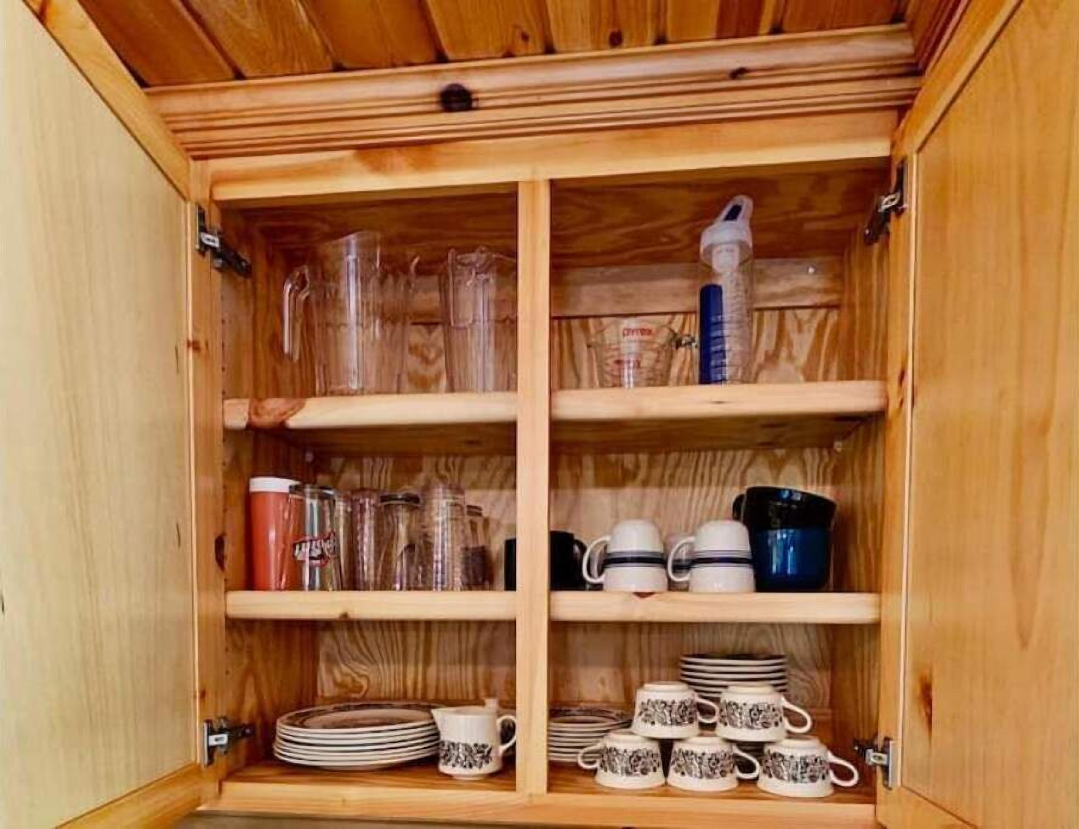 A wooden cabinet with shelves containing glass jars, measuring cups, and stacked plates and cups.