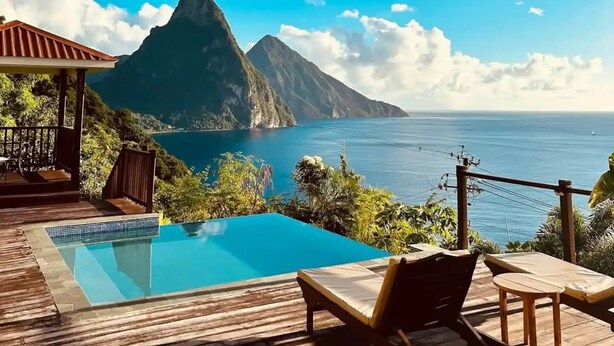 Una terraza de madera con piscina, sillas de descanso y vista a la montaña y al océano.