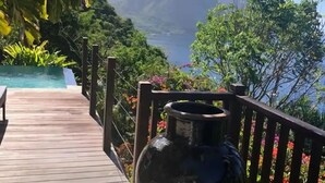 Una terraza de madera con un jarrón grande, con vista a un paisaje montañoso y una masa de agua.