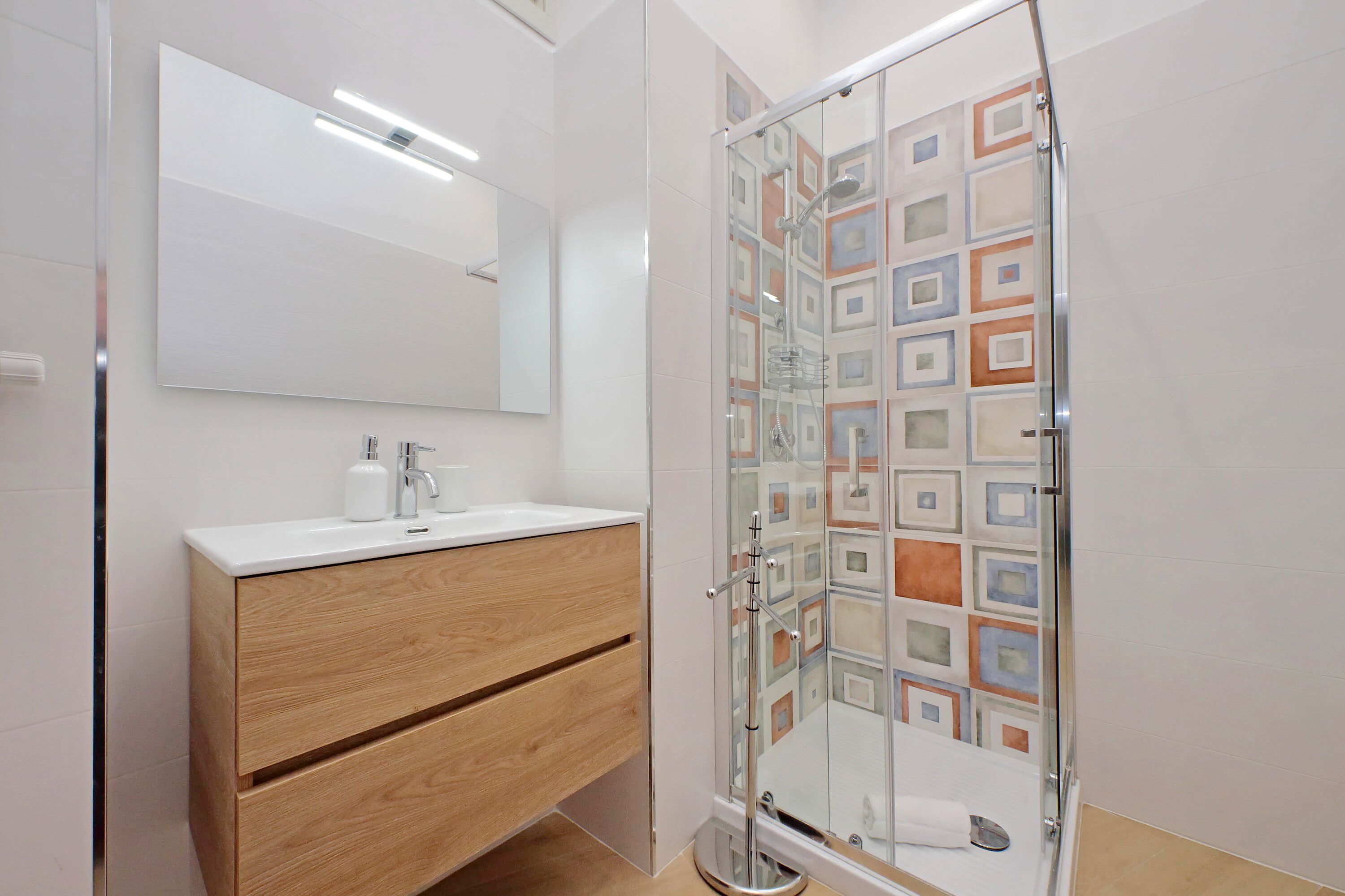 Une salle de bain moderne avec une douche à parois de verre, un meuble-lavabo en bois et un grand miroir.