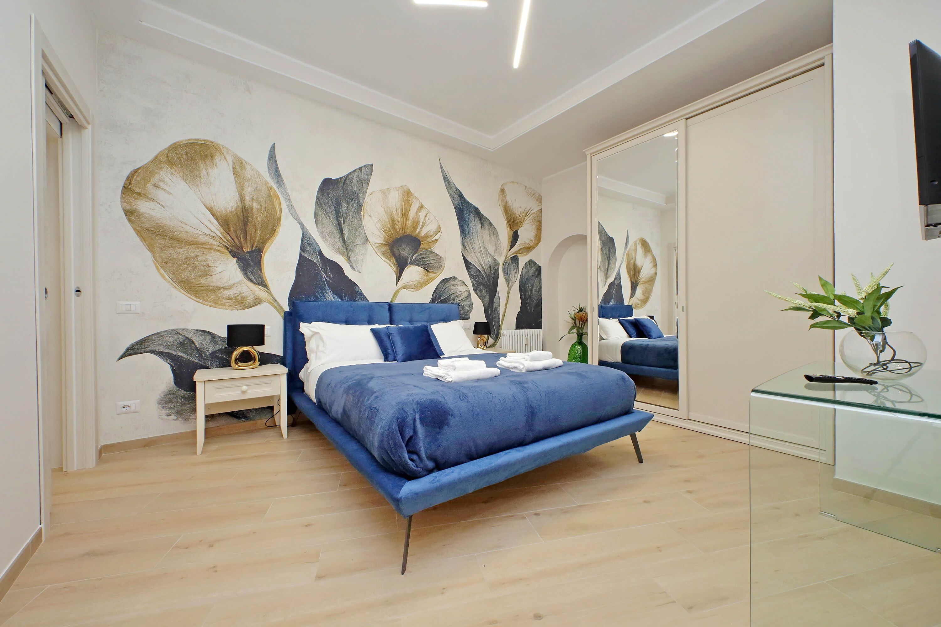 Un dormitorio moderno con una cama grande, un escritorio de cristal y un mural en la pared.