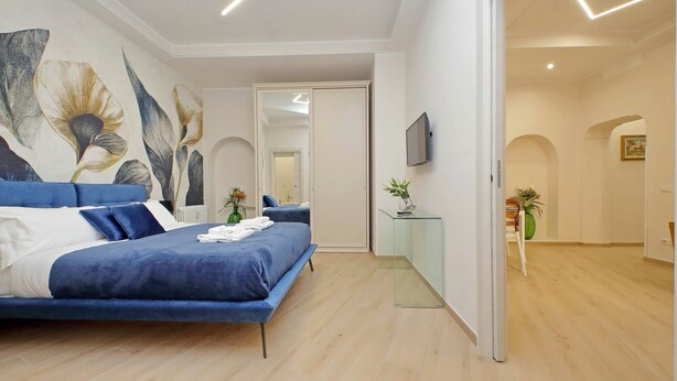 Ein modernes Schlafzimmer mit einem großen Bett, einem Glastische und einem an der Wand befestigten Fernseher.