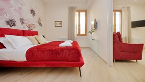 A hotel room with a red bed, a glass partition, a red armchair, a TV, and a window with curtains. - 4BNB - Ottaviano Vatican Flat - Red (Rome)