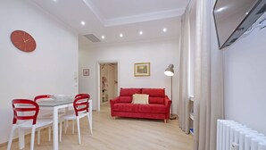 A modern living room with a dining area, a red sofa, and a white radiator. - 4BNB - Ottaviano Vatican Flat - Red (Rome)