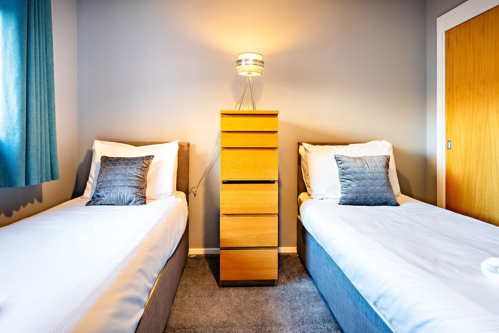 A hotel room with two single beds, a wooden dresser, and a wall-mounted lamp.