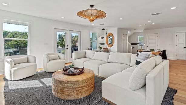 A spacious living room with a large sectional sofa, a round coffee table, and a modern chandelier. - The Twin Palms at Vilano Beach,  Private Pool - Steps From Beach - Minutes from everything (Vilano Beach)
