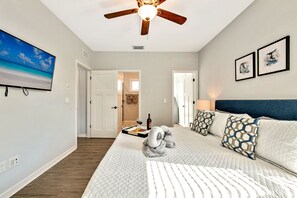 Un dormitorio con cama, ventilador de techo, televisión y obras de arte en la pared.