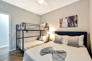 Een kamer met stapelbedden, een nachtkastje met een lamp, een schilderij aan de muur en een groot bed met veel kussens.