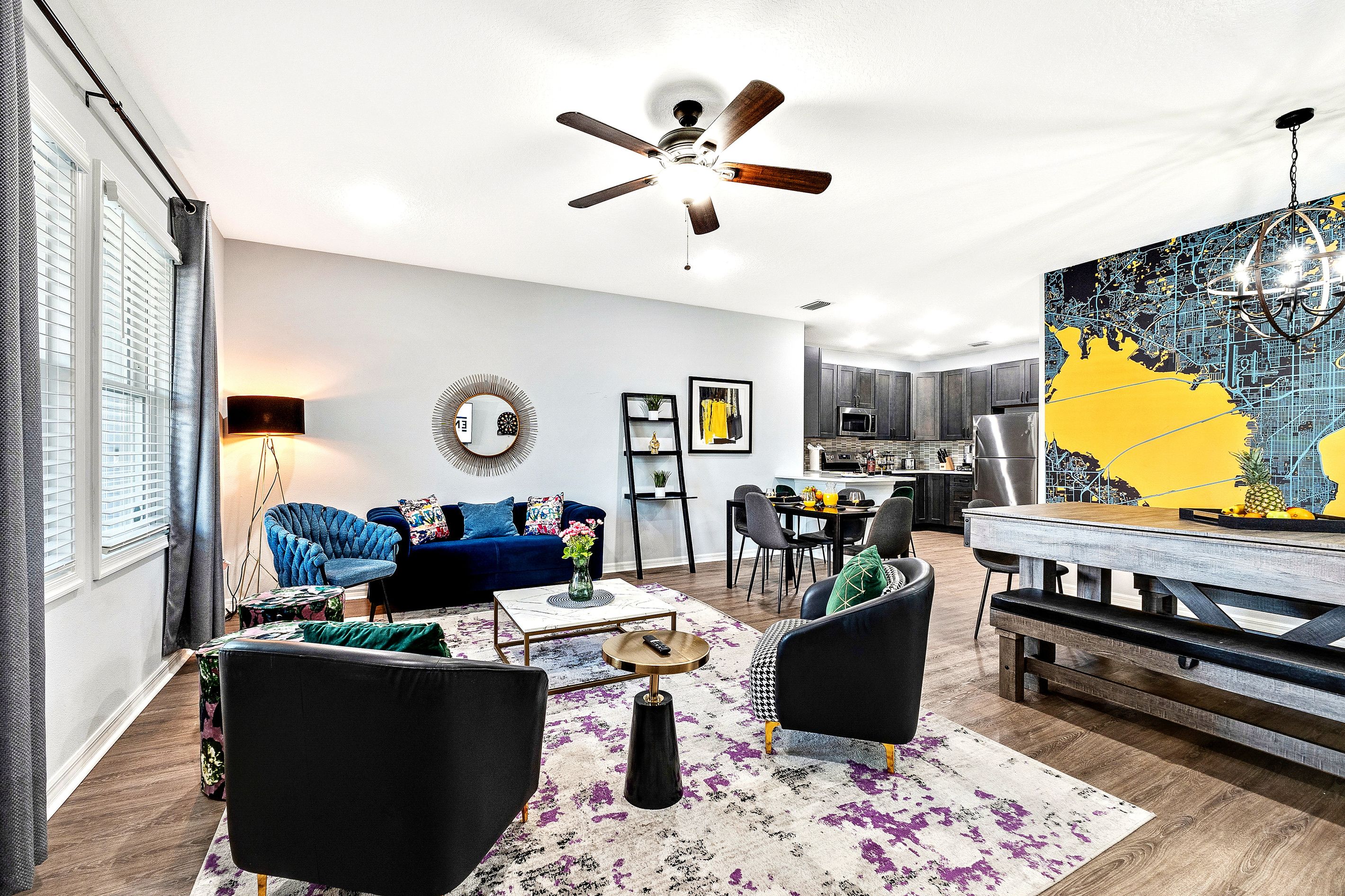 Un salon moderne avec un canapé bleu, des fauteuils noirs, une table basse et un coin repas agrémenté d’une fresque représentant une carte.