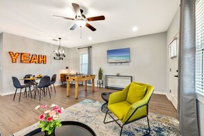 Een moderne woonkamer met een tafelvoetbalspel, een felgele fauteuil en een plafondventilator.