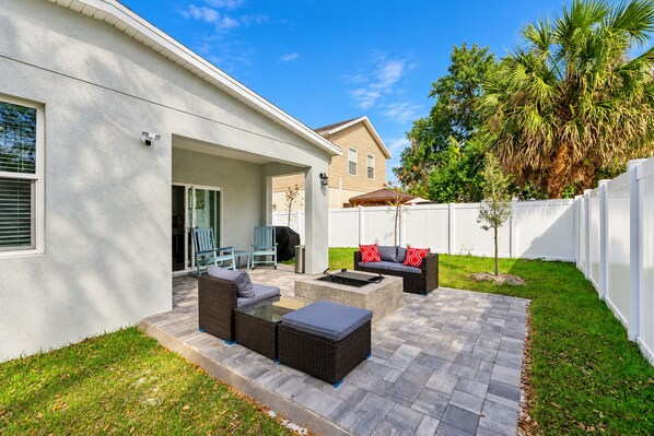 A patio with outdoor furniture, a barbecue grill, and a white fence.