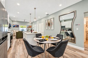 A modern kitchen with a dining area, featuring a central island, black chairs, and a large mirror.