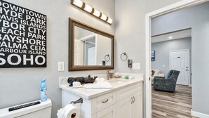 Un baño con tocador blanco, un espejo grande y una lámpara fijada a la pared.
