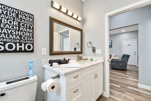 A bathroom with a white vanity, a large mirror, and a wall-mounted light fixture.