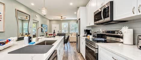 A modern kitchen with white cabinetry, stainless steel appliances, and a marble countertop.