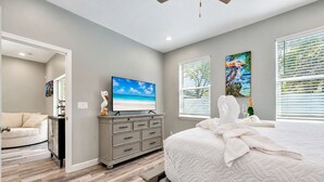 Un dormitorio con cama, cómoda, televisión y obras de arte en las paredes.