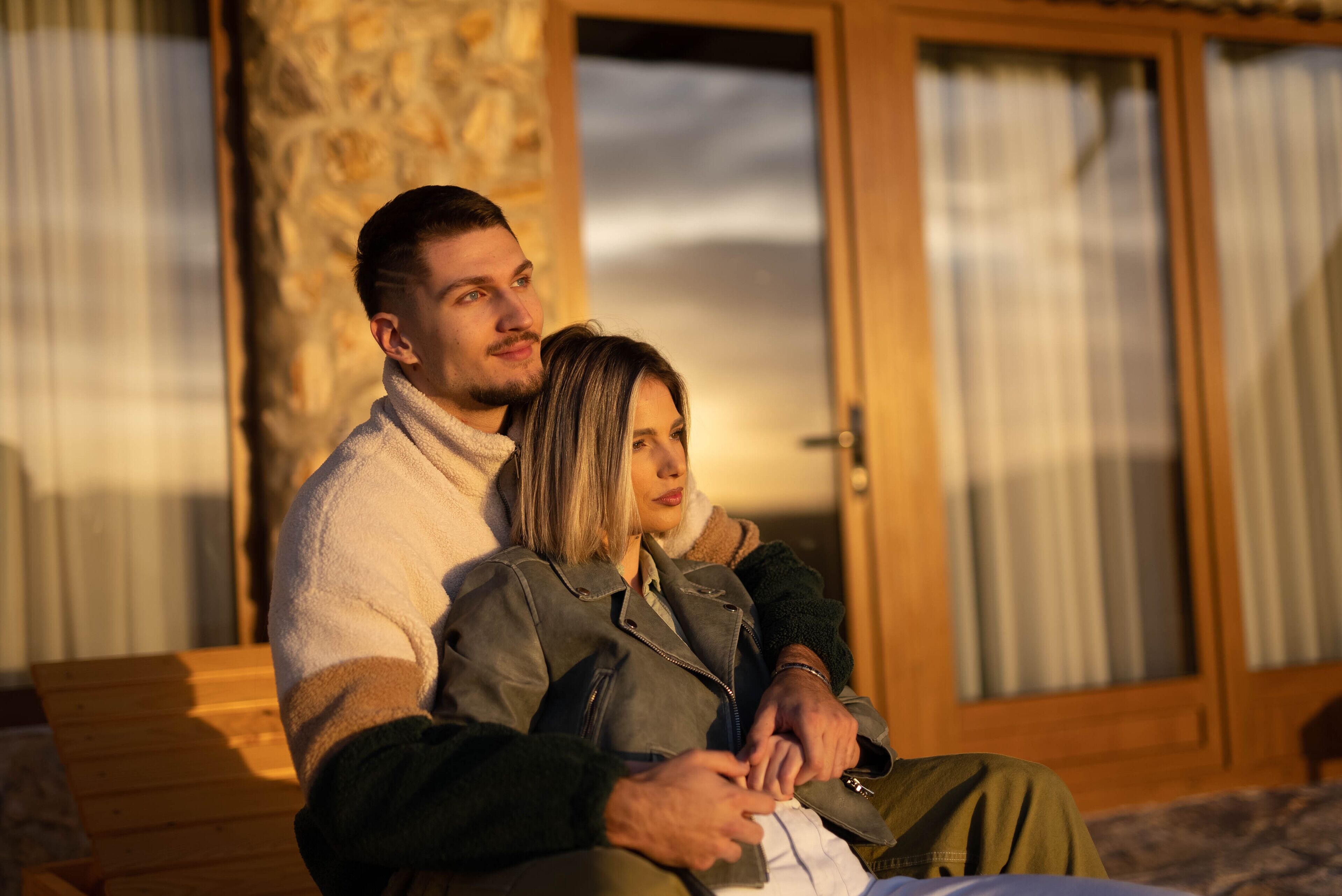 A couple sitting on a bench in a room with a stone wall and a wooden door.