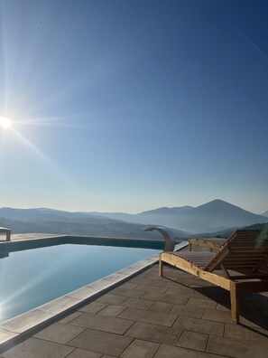 Une piscine à débordement offrant une vue imprenable sur les montagnes et une terrasse en bois avec des chaises longues.