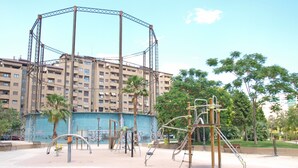 Ein Spielplatz mit diversen Geräten, einer Palme und einem Gebäude im Hintergrund.