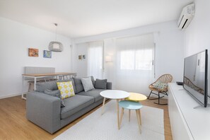 A modern living room with a grey sofa, a small dining table, a TV, and a wicker chair. - Port Area II. WiFi + Air Condition (Valencia)