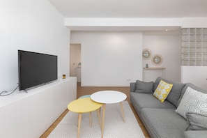 A modern living room with a flat-screen TV, a grey sofa, a small round table, and a patterned rug. - Port Area II. WiFi + Air Condition (Valencia)