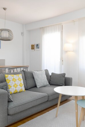 Ein modernes Wohnzimmer mit einem grauen Sofa, einem runden weißen Tisch und einer hängenden Pendelleuchte.