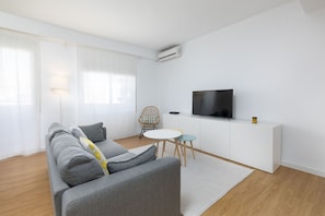 Ein modernes Wohnzimmer mit grauem Sofa, einem kleinen runden Tisch und einem Fernseher auf einem weißen Schrank.