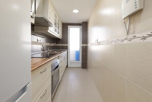 A narrow kitchen with white cabinets, stainless steel appliances, and a tiled backsplash. - Port Area II. WiFi + Air Condition (Valencia)
