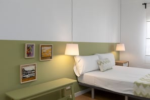 Ein Schlafzimmer mit einem Bett, zwei Nachttischlampen, einer Bank und drei gerahmten Kunstwerken an der Wand.