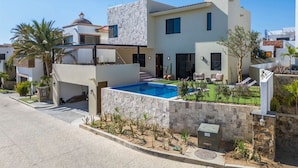 Ein modernes, zweigeschossiges Haus mit Swimmingpool, Steinmauern und einem gepflegten Garten.