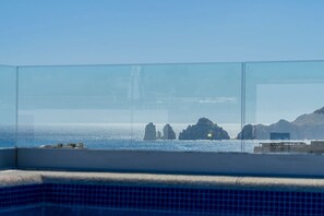A clear view of the sea with rock formations, a distant building, and a pool area with tiled flooring. - Casa Torote - Best Rooftop Views (Cabo San Lucas)