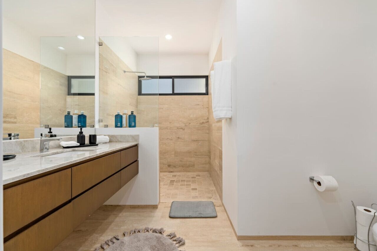 A modern bathroom with a large mirror, a shower, and a toilet.