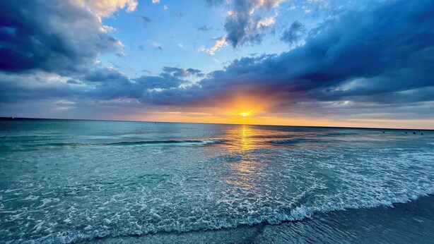 Una playa con el sol poniéndose sobre el océano, creando un reflejo en el agua.