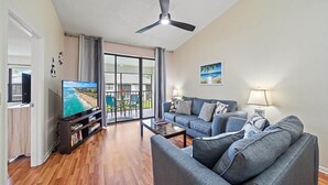Una sala de estar con televisión, sof á, mesa de centro y ventilador de techo.