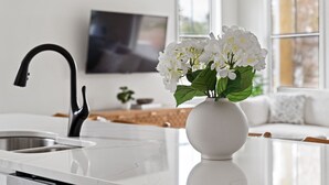 Une cuisine moderne avec un plan de travail en marbre blanc, un robinet noir et un vase blanc contenant des fleurs blanches.