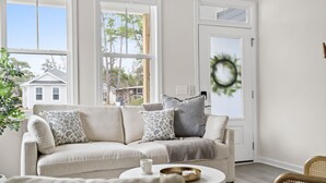 Un salon chaleureux avec un canapé d’angle beige, une table basse ronde et un fauteuil en osier.