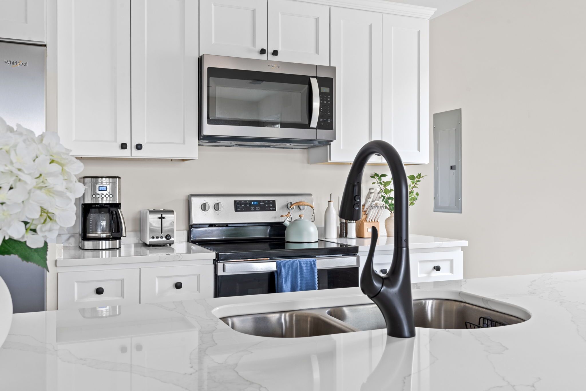 A modern kitchen with white cabinets, a stainless steel microwave, a coffee maker, a toaster, and a kettle.