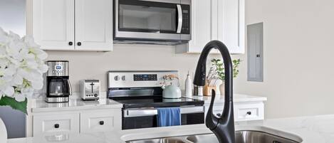 A modern kitchen with white cabinets, a stainless steel microwave, a coffee maker, a toaster, and a kettle.