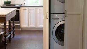 Una cocina con lavadora de doble puerta, suelo de madera y muebles de cocina blancos.