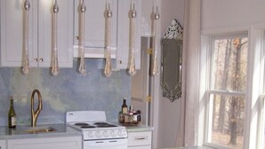A modern kitchen with white cabinets, a marble countertop, and a central island with bar stools. - Glasshouse in the Woods. Five acres of wooded privacy and wildlife. (Augusta)