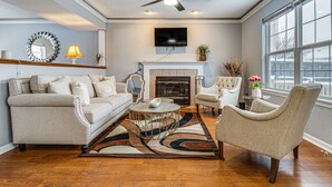 A living room with a fireplace, a ceiling fan, and a large window. - Indianapolis Home w/ Private Yard ~ 8 Mi to Dtwn! (Indianapolis)