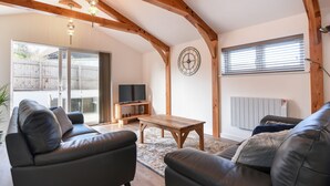 A living room with a TV on a wooden stand, leather sofas, a wooden coffee table, and a large clock on the wall. - The Stables @ Merrydown (Axminster)