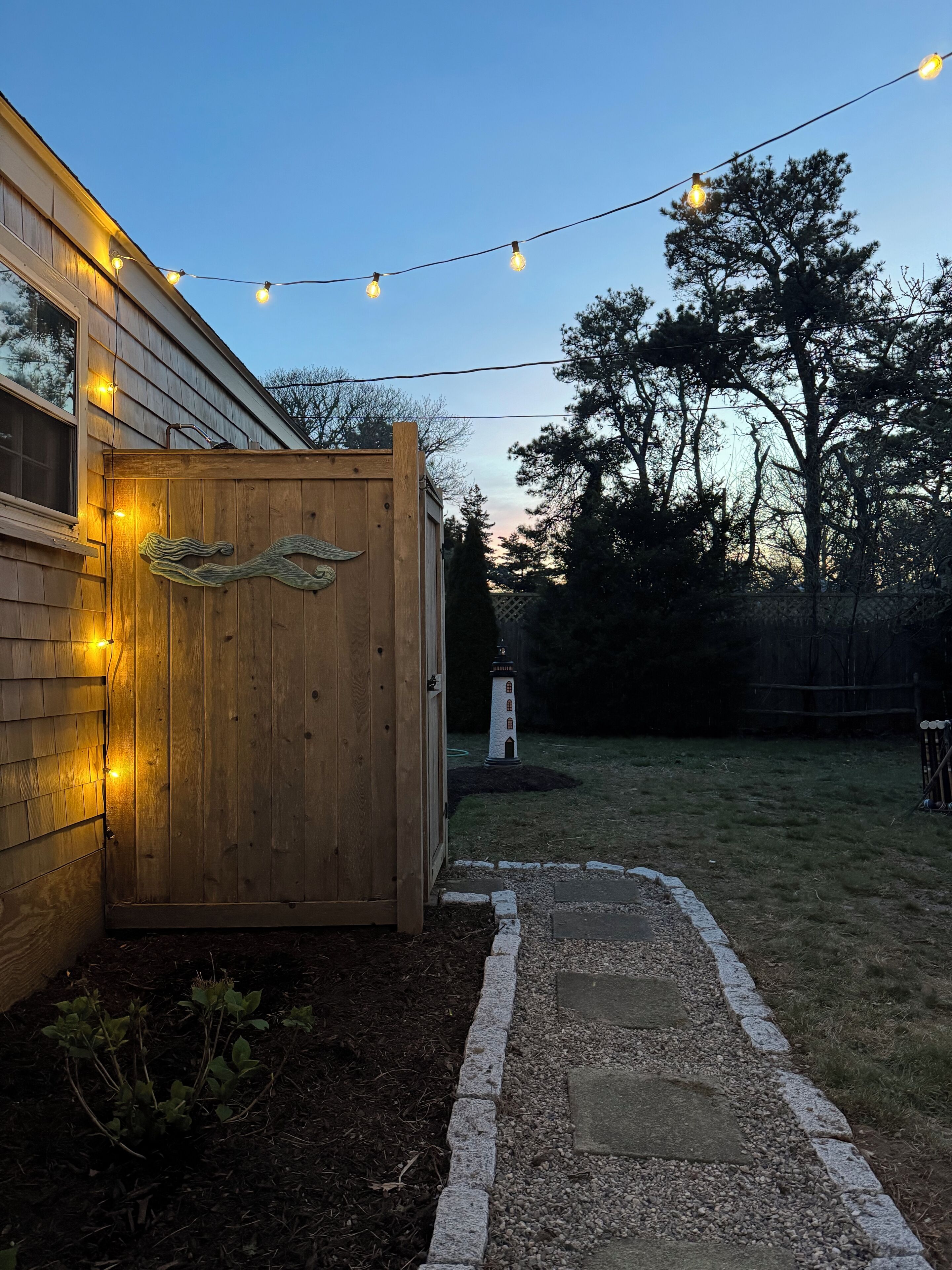 A wooden gate with a decorative design, a pathway leading to a house, and a string of lights in a backyard.