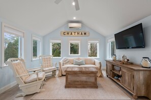 A living room with a beige sofa, two rocking chairs, a wooden coffee table, and a TV on the wall.