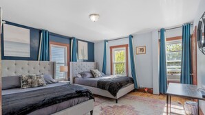 A bedroom with two beds, a large window with curtains, a ceiling light, and a rug.