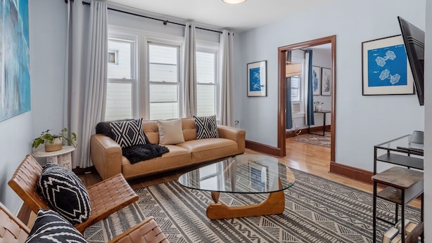 A modern living room with a leather sofa, a glass coffee table, and a patterned rug.