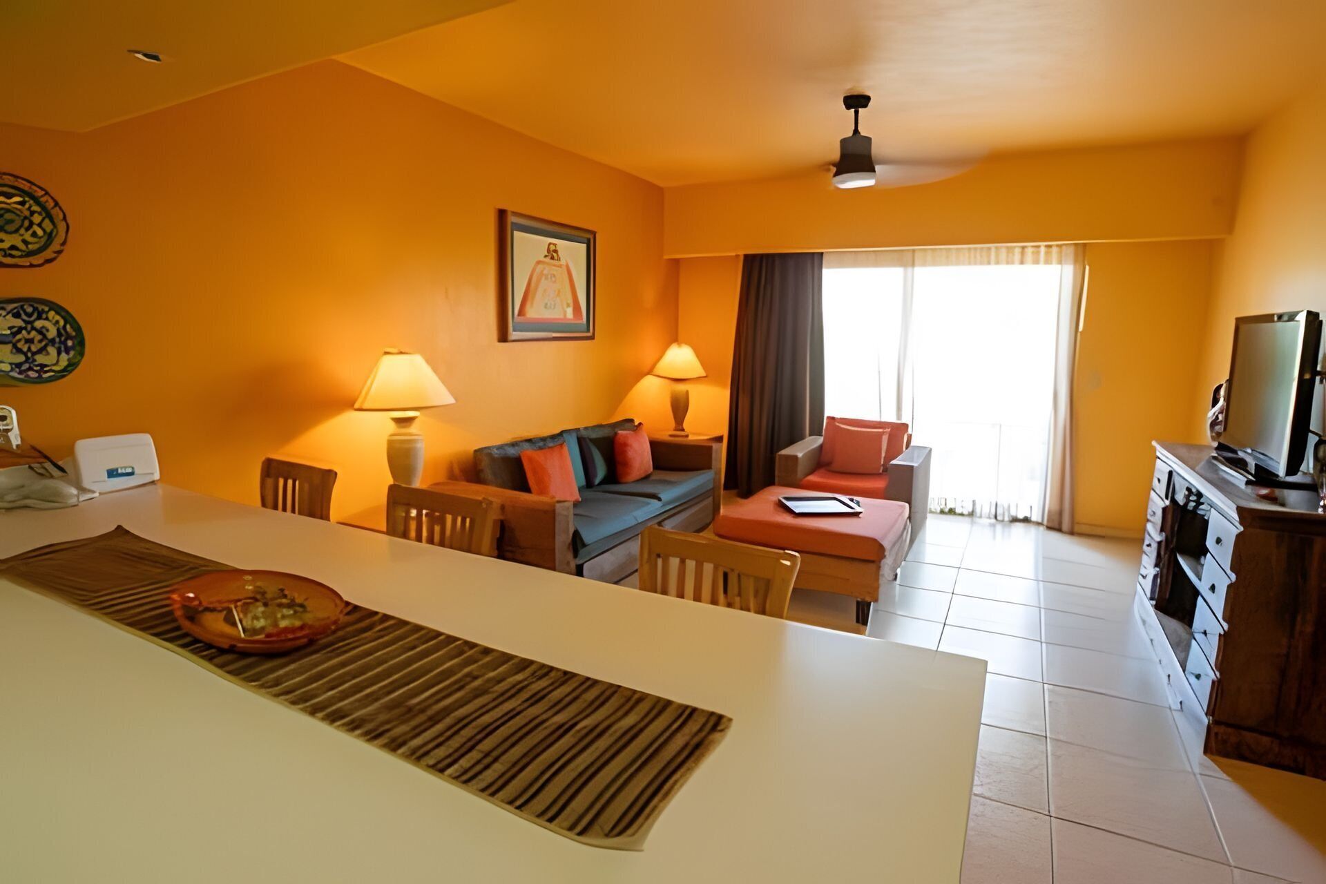 A hotel room with a dining area, a sofa, a TV, and a large window.