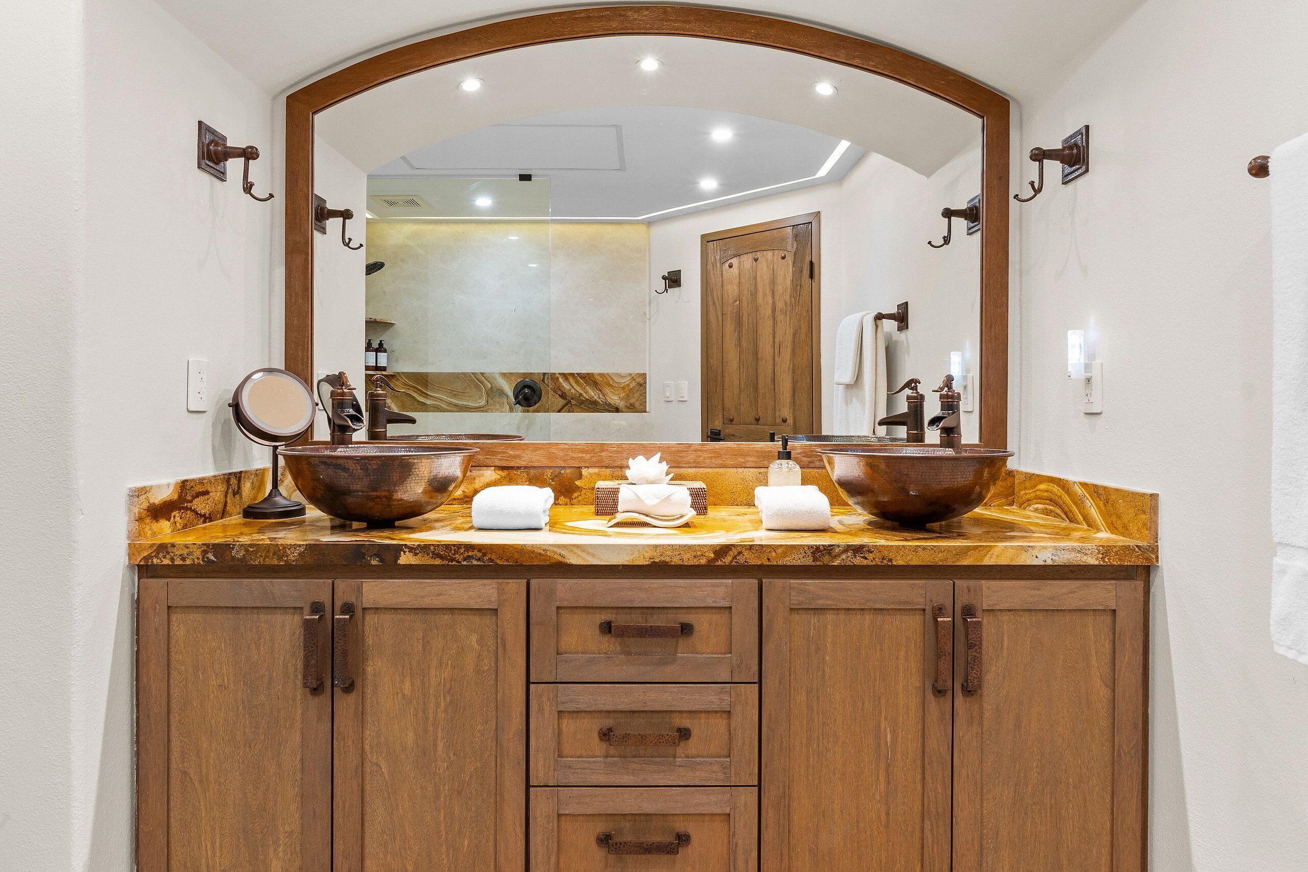 A bathroom with a wooden vanity, two sinks, a large mirror, and a wooden door.